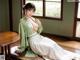 A woman in a green kimono sitting on a wooden floor.