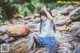 A woman sitting on a rock in a stream.