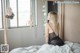 A woman sitting on a bed looking out a window.