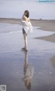 A woman standing on a beach with her reflection in the water.