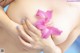 A woman holding a pink flower in her breasts.