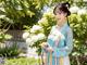 A woman in a blue and yellow dress standing in front of a bush.